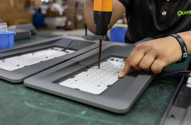 Worker assembling LED light modules for solar street lights using electric screwdriver